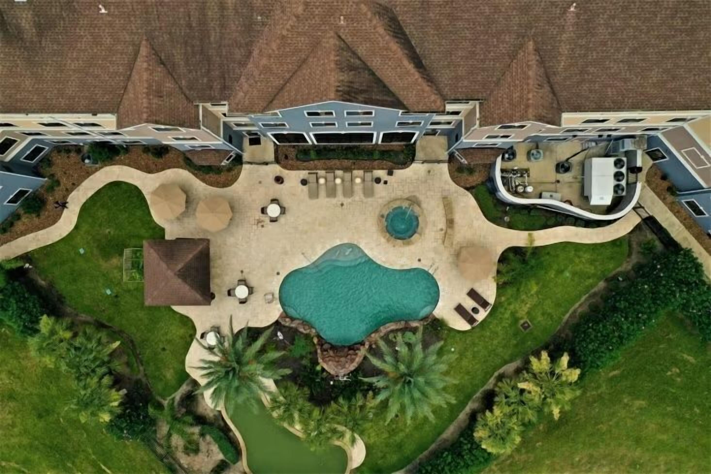An aerial view of a resort with a central swimming pool, multiple guest rooms, and landscaped gardens.