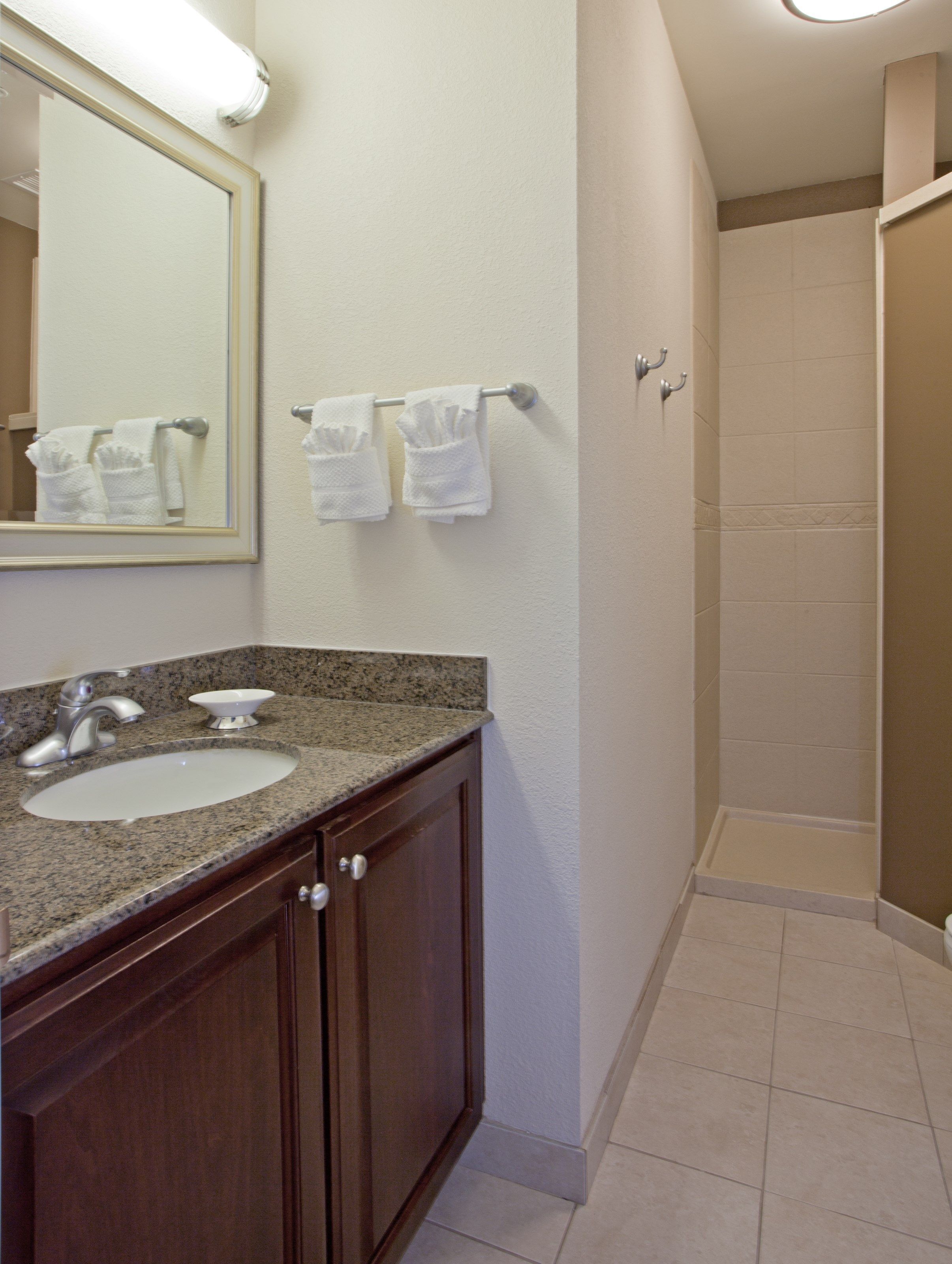 A bathroom with a granite countertop sink, a mirror, and a shower stall.