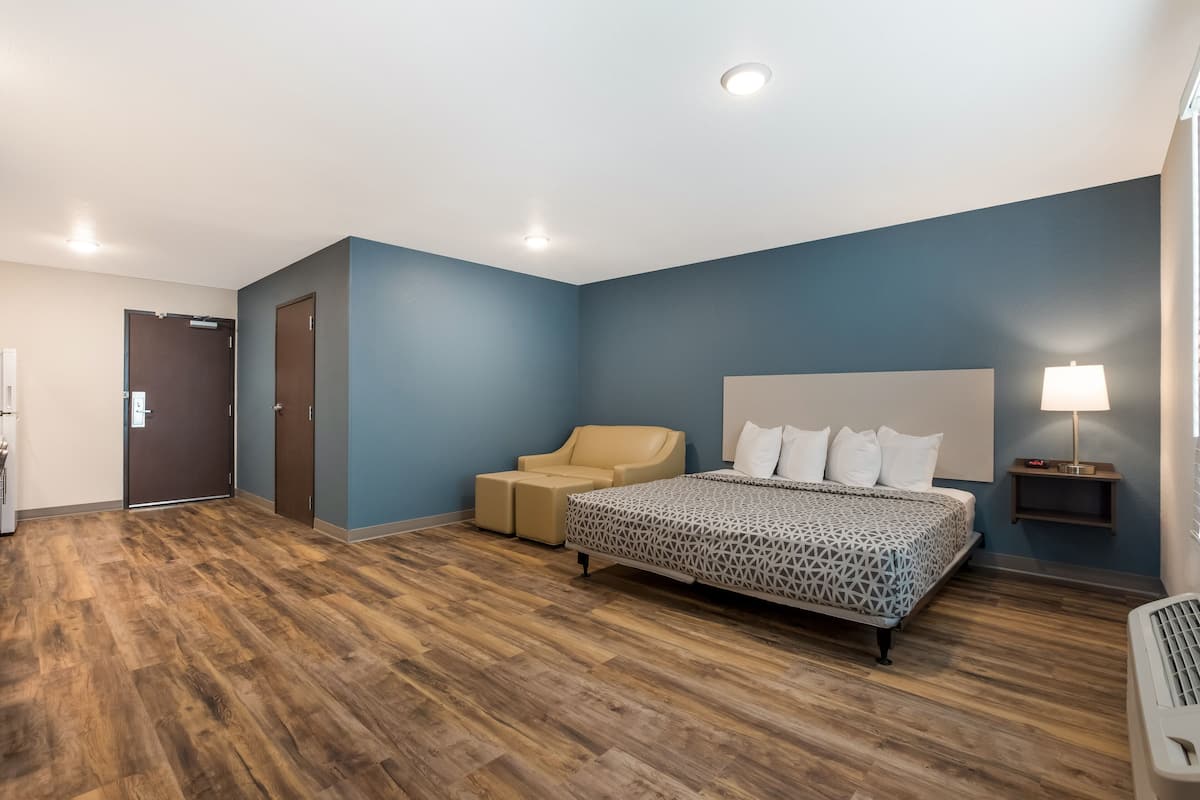 A hotel room with a bed, a chair, a bedside table with a lamp, and a door.