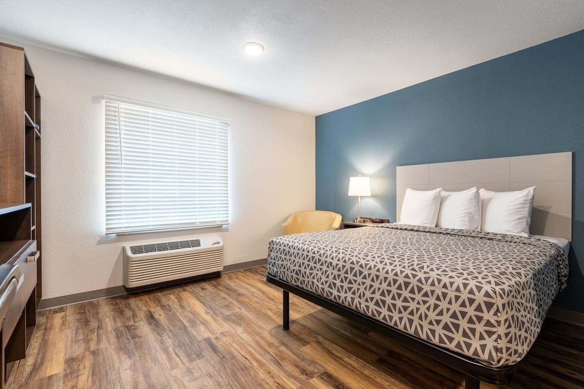 A hotel room with a bed, a chair, a desk, a lamp, and a window with blinds.