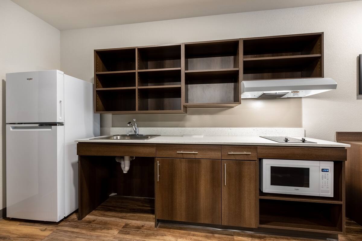 A kitchen with a built-in microwave, a refrigerator, wooden cabinets, and a sink.