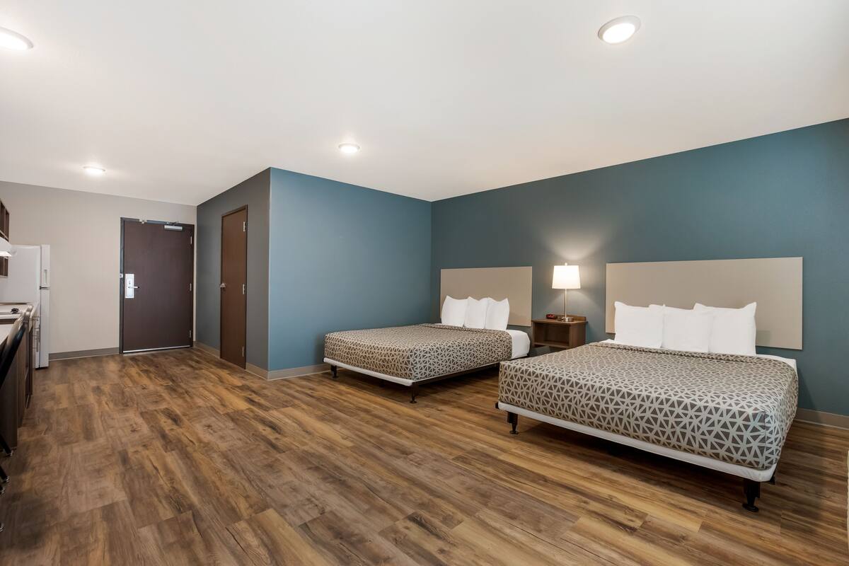 A hotel room with two beds, a kitchenette, and a bathroom.