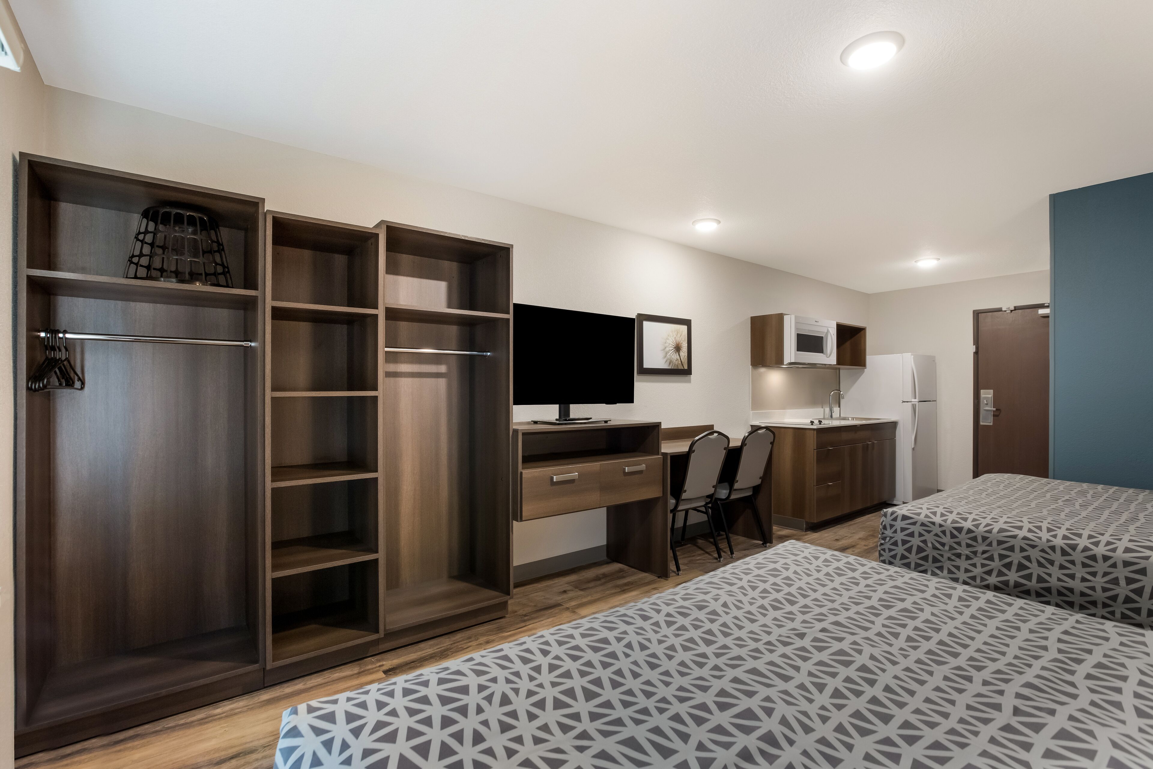 Habitación compacta con cama, escritorio, silla, armario, televisor y kitchenette.