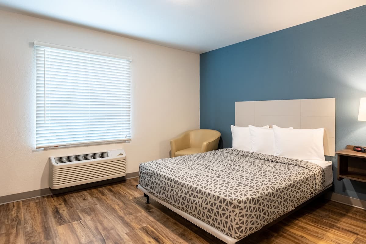 A bedroom with a bed, a chair, a heater, and a window with blinds.