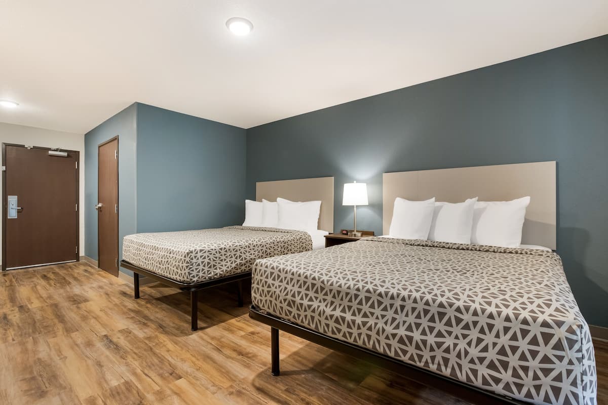 A hotel room with two beds, wooden flooring, and a door.