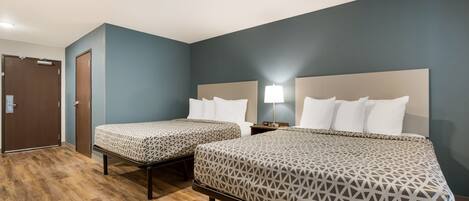 Quarto de hotel com duas camas, piso de madeira e uma porta.