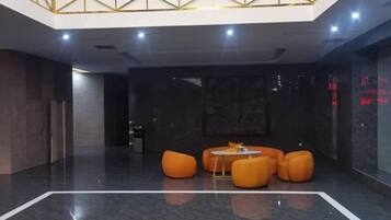 A lobby with a high ceiling, a marble floor, and orange seating.