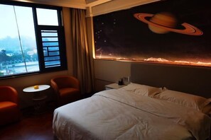 A hotel room with a large window, a bed, a small round table, two armchairs, and a wall mural of a planet with rings. - Zhenfeng Hotel (Zhenfeng)