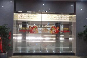 L’entrée d’un hôtel, avec une porte en verre, une enseigne avec des caractères chinois et des plantes en pot de chaque côté.
