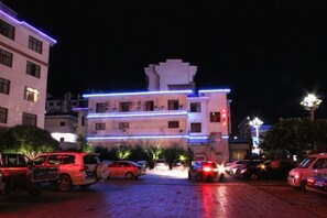 Un edificio de varios pisos con un estacionamiento frente a él, iluminado con luces artificiales.