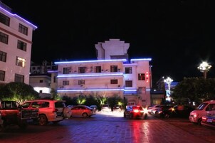 Un edificio de varios pisos con un estacionamiento frente a él, iluminado con luces artificiales.