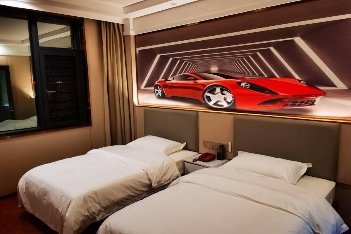 Quarto de hotel com duas camas, uma janela e uma obra de arte na parede retratando um carro esportivo vermelho.