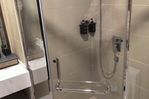 Ducha con cerramiento de vidrio, cabezal de ducha de mano, grifo empotrado en la pared y dos dispensadores de jabón negros.