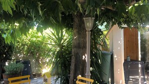 Eine Terrasse mit rundem Tisch und zwei gelben Stühlen, umgeben von Steinplatten und Grünpflanzen.