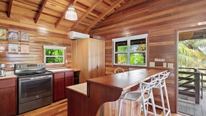 A kitchen with wooden walls, a stainless steel oven, a bar area with white stools, and a window with a view of greenery.