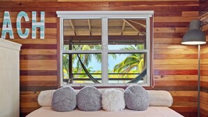 Un dormitorio con pared de madera, una ventana con vista a palmeras y una cama con cinco almohadas.