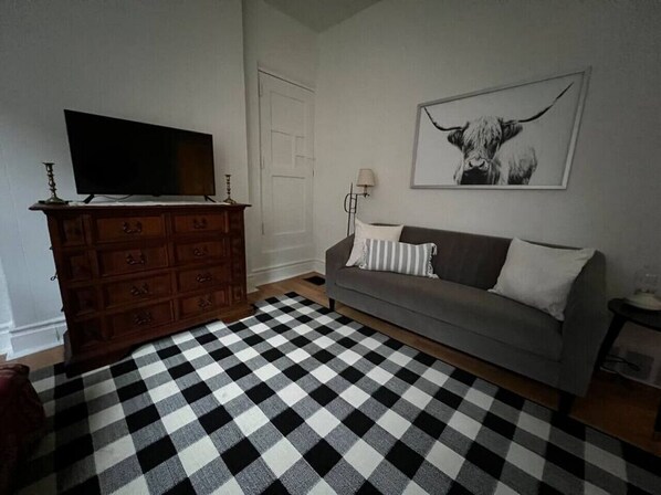 A living room with a checkered floor, a grey sofa, a wooden dresser, and a framed picture on the wall.