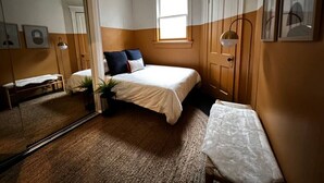 A bedroom with a bed, a window, a mirror, and a bedside table.