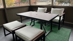 A sunroom with a table and chairs, a view of the neighborhood, and a green artificial turf floor.