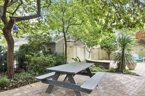 A picnic table in a garden with a wooden fence and a potted plant in the background. - Charming Yellow Cottage in Dilworth! (Charlotte)