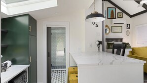 Une cuisine moderne avec un îlot en marbre blanc, des armoires vertes et un tabouret jaune. On y trouve également une chaise noire et un canapé jaune dans l’espace repas.