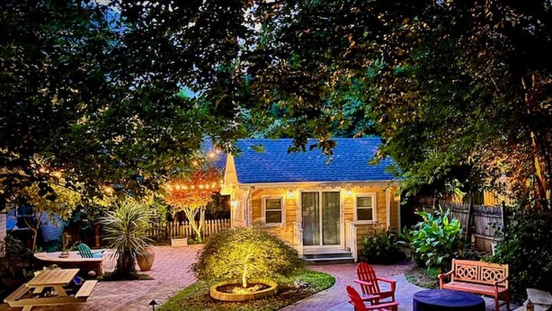 Une maison avec un toit bleu, un porche à l’avant et un jardin agrémenté d’un foyer et d’un espace détente.