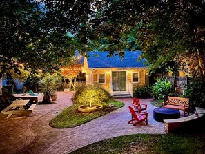 A house with a blue roof, a front porch, and a garden with a fire pit and seating area. - Charming Yellow Cottage in Dilworth! (Charlotte)