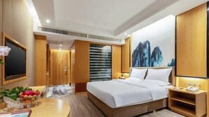 Una habitación de hotel moderna con una cama grande, muebles de madera, un televisor de pantalla plana y un cuadro de montañas en la pared.