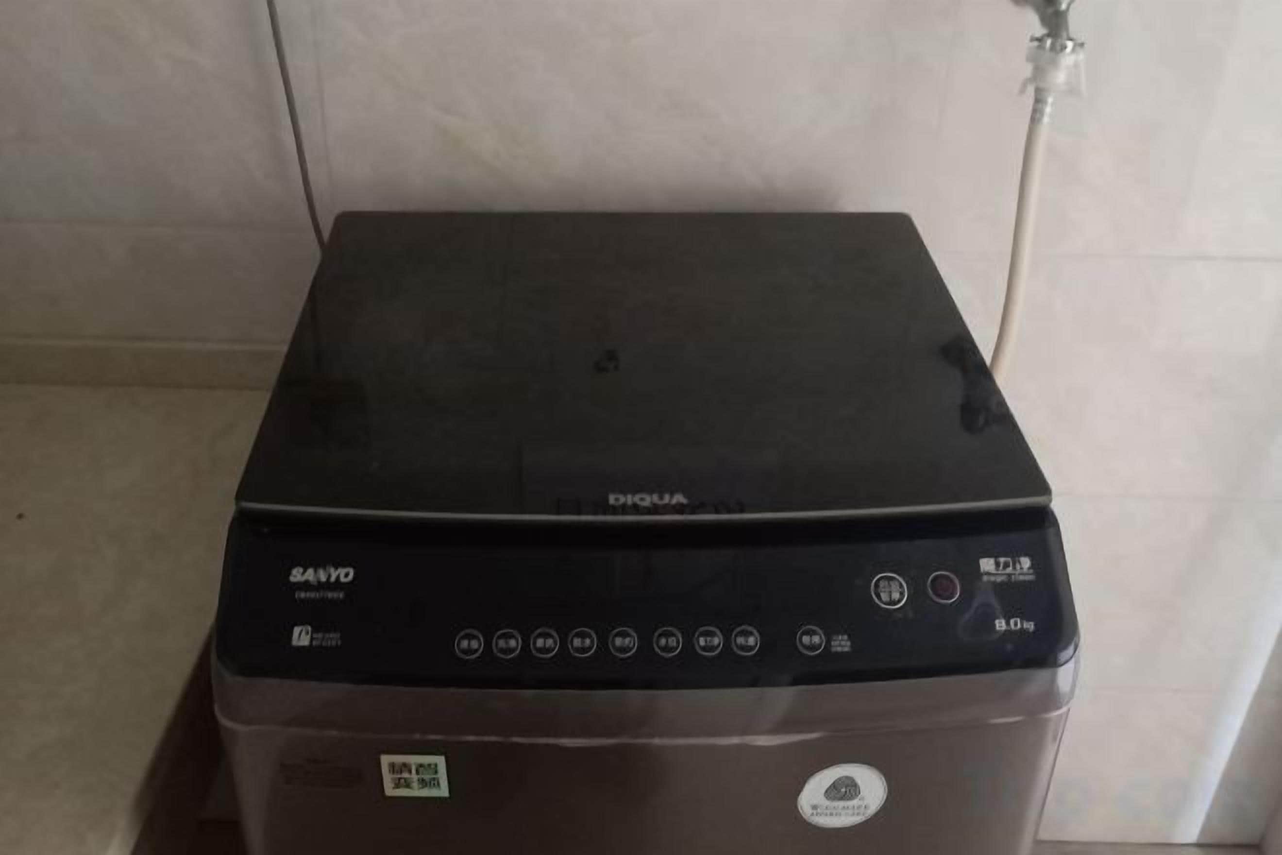Een zwarte wasmachine met bedieningspaneel, een merklabel en een waterslang.