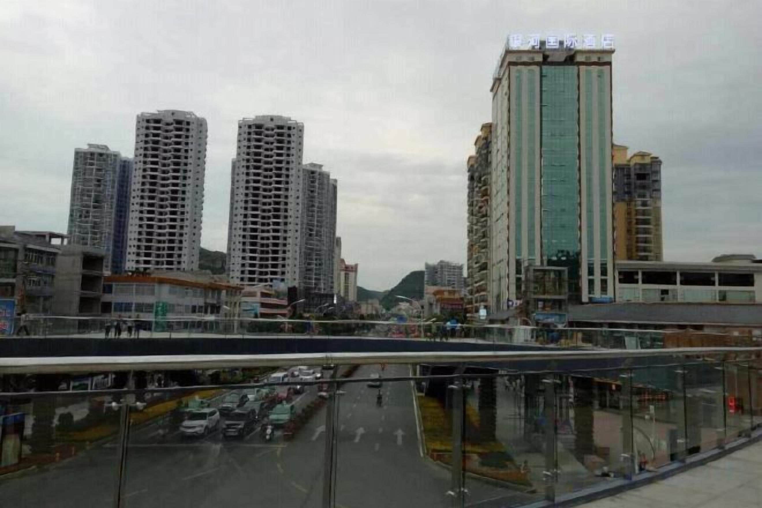 Un paisaje urbano con rascacielos, un puente de cristal y una calle con vehículos.