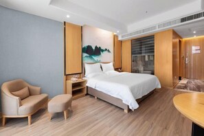 A modern hotel room with a large bed, a wooden nightstand, a beige armchair, and a small table. - Galaxy International Hotel (Zhenning)