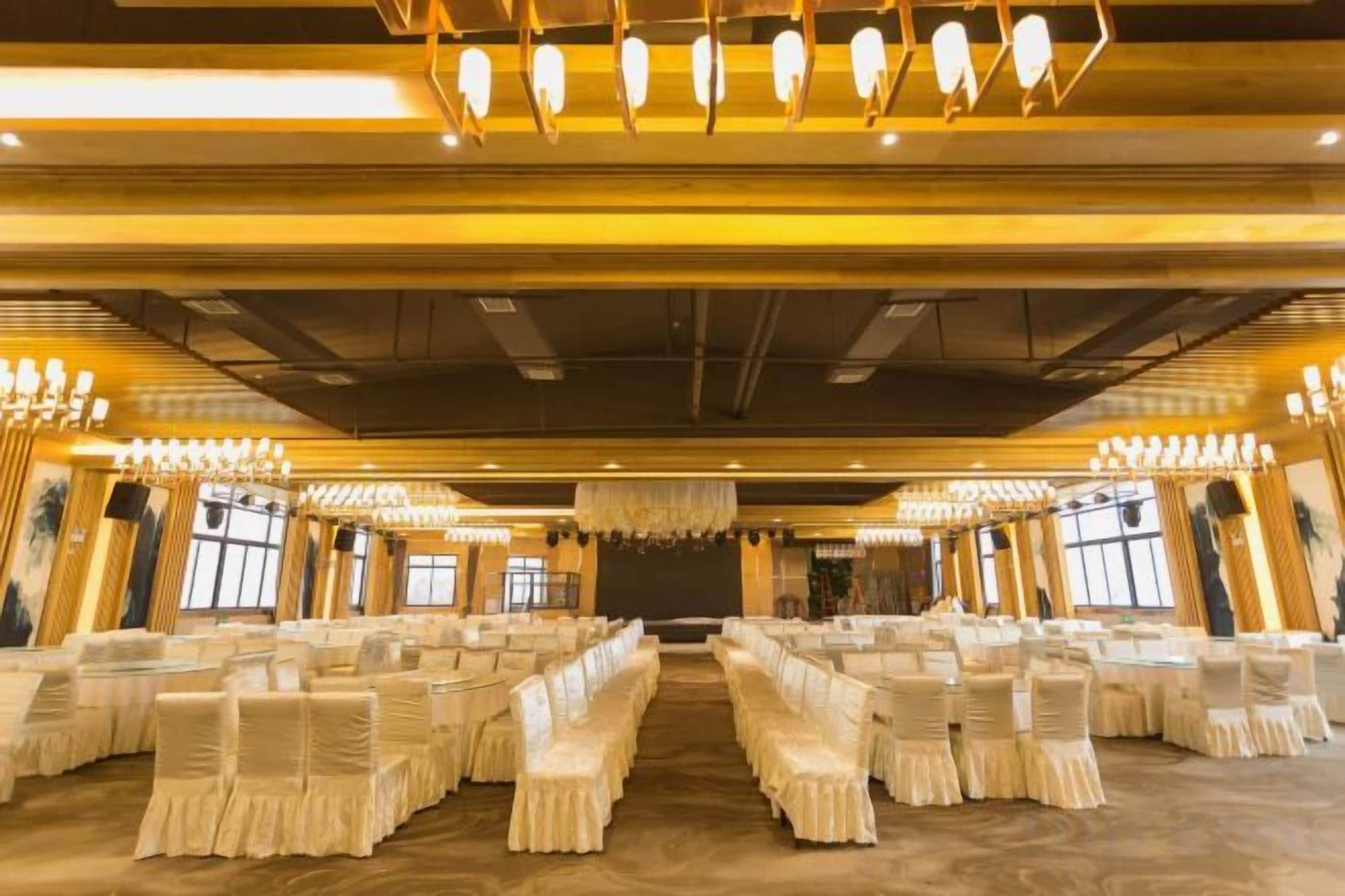 A banquet hall with rows of tables and chairs, chandeliers, and a stage at the front.