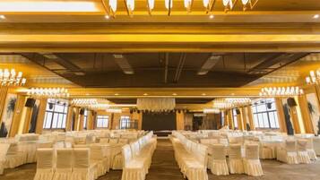 A banquet hall with rows of tables and chairs, chandeliers, and a stage at the front.