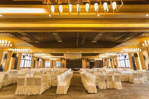 A banquet hall with rows of tables and chairs, chandeliers, and a stage at the front. - Galaxy International Hotel (Zhenning)