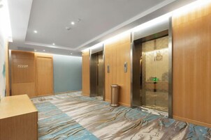 Un vestíbulo de hotel con alfombra de diseño de mármol, paneles de madera y dos ascensores.