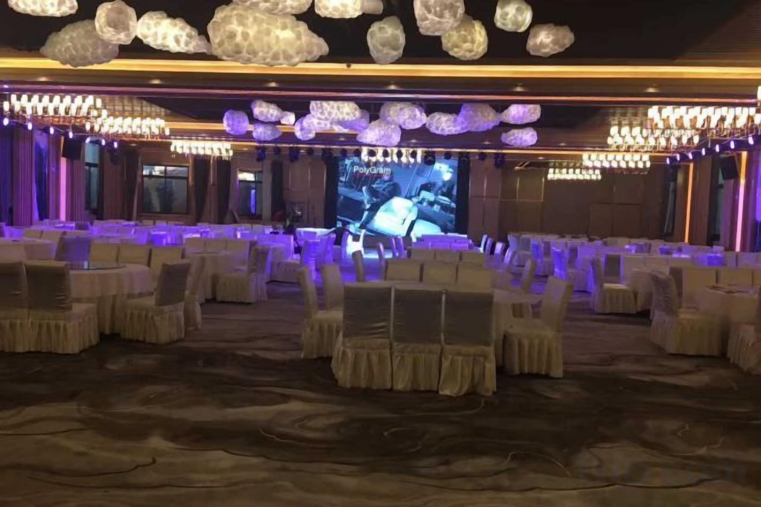 A banquet hall with rows of tables and chairs, a large screen, and chandeliers.
