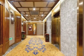 Un pasillo de hotel con puertas de madera, alfombra estampada y pared de mármol.