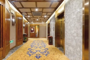 Corredor de hotel com portas de madeira, carpete estampado e parede de mármore.