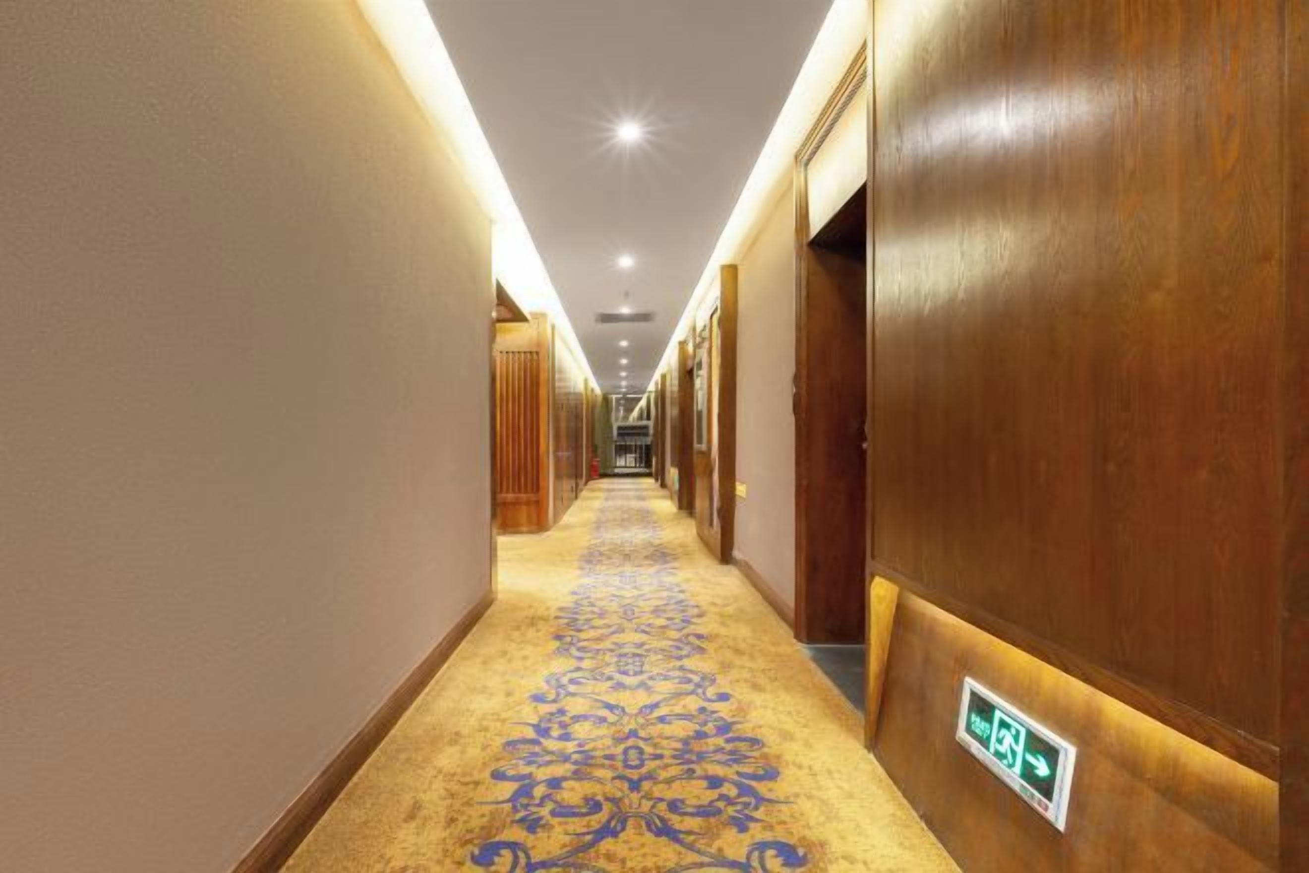 A hotel corridor with a carpeted floor, wooden walls, and a sign indicating an emergency exit.