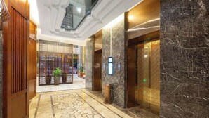 Un vestíbulo de hotel con piso de mármol, paneles de madera, un mostrador de recepción y un ascensor.