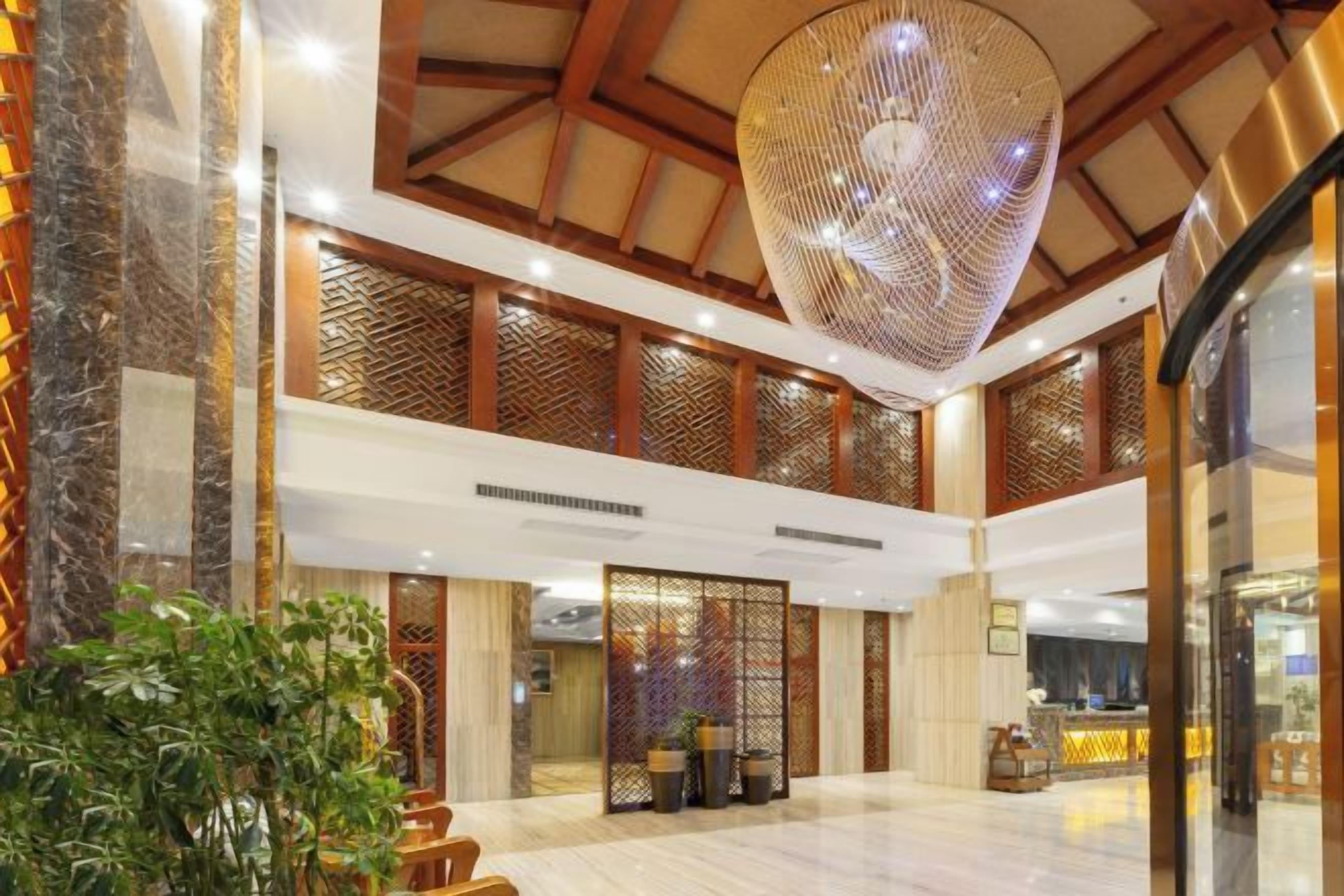 Un hall d’entrée spacieux avec un plafond haut, un grand lustre suspendu et un comptoir de réception.