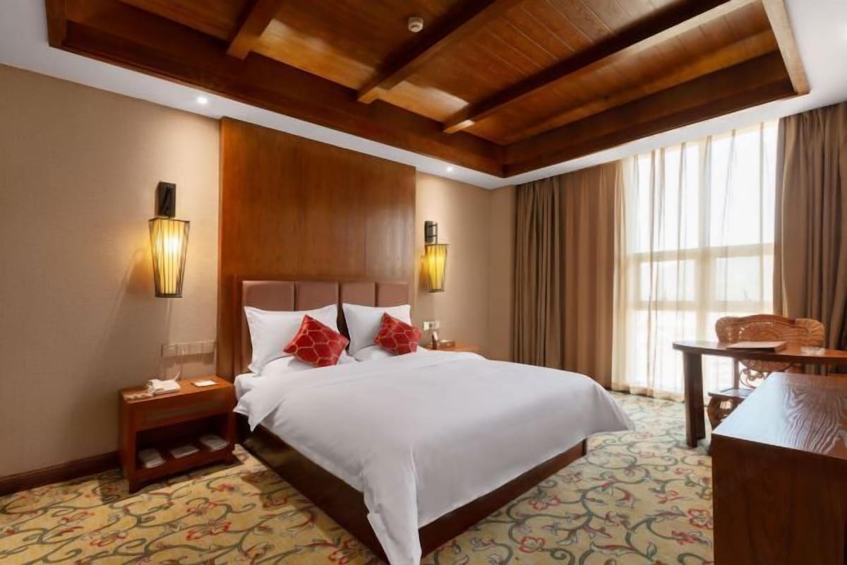 A hotel room with a large bed, two bedside tables, a desk, and a window with curtains.