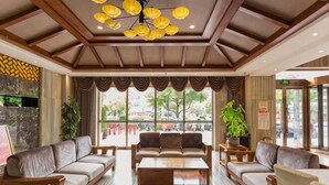 Un vestíbulo de hotel con techo de madera, ventanas amplias y un área de descanso con sofás y una mesa de centro.