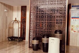 Un vestíbulo de hotel con piso de madera, un separador decorativo, un carrito y varios botes de basura.