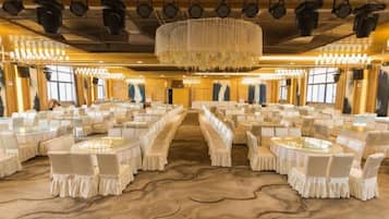 A banquet hall with round tables and chairs, a central aisle, and a chandelier.