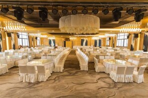 Un salón de banquetes con mesas redondas y sillas, un pasillo central y una araña.