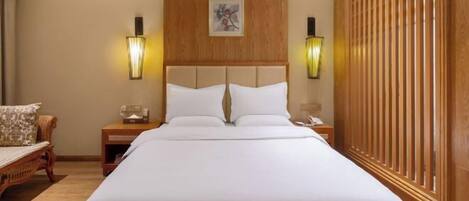 A hotel room with a large bed, wooden headboard, two bedside tables with lamps, a wooden wardrobe, and a wall-mounted artwork.
