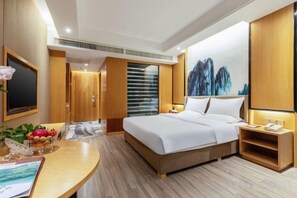 A hotel room with a large bed, a desk with a computer, a TV, and a painting on the wall. - Galaxy International Hotel (Zhenning)