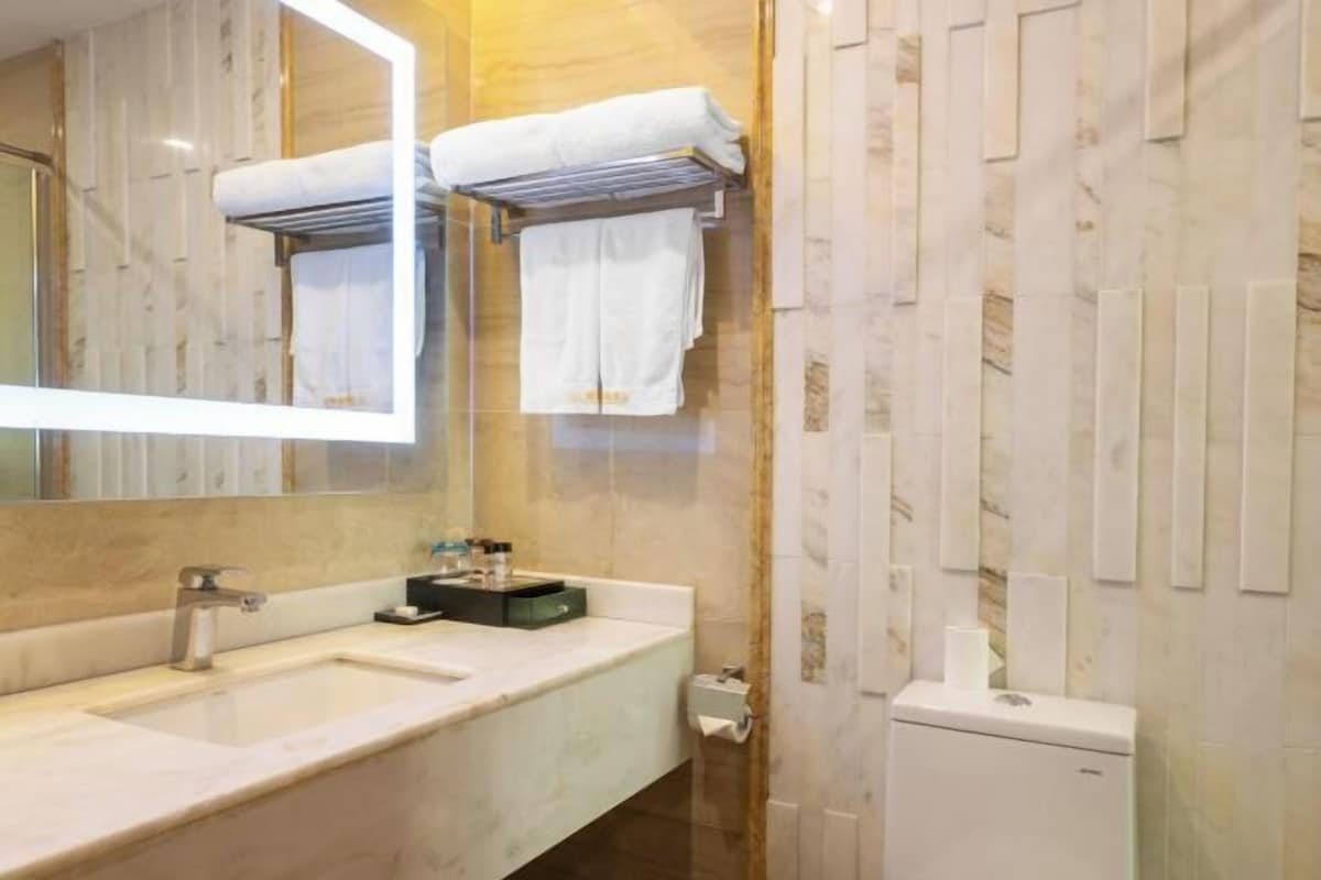A bathroom with a large mirror, a sink, and a toilet. There are towels hanging on a rack.