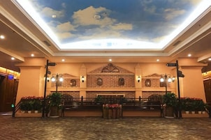 Um saguão de hotel com teto alto, parede de tijolos com padrão decorativo e balcão de recepção.